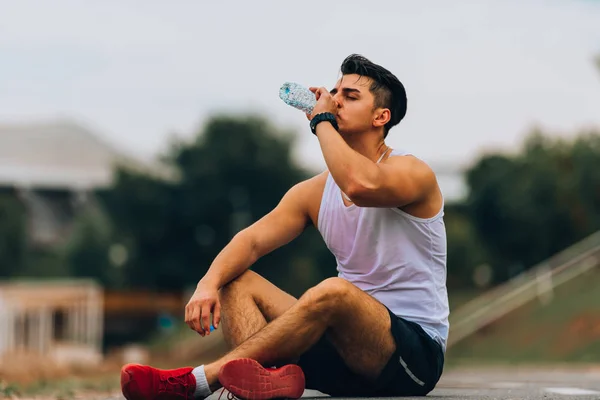 Man in mouwloos drinkwater na het uitvoeren van workout op het strand — Stockfoto