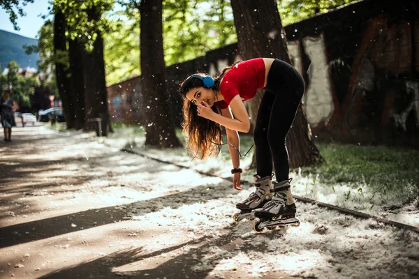 Woman lacing up rollers while standing in the park and listening — Stock Photo, Image