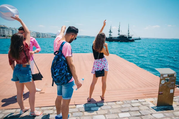 Vier Touristen winken einem alten schwarzen Piratenboot zu, das vorbeifährt — Stockfoto