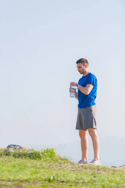 Αθλητής φορώντας ένα μπλε πουκάμισο και γκρι σπορ σορτς πίνει νερό — Φωτογραφία Αρχείου
