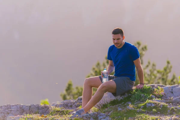 英俊的运动员坐在岩石峰,而看着br — 图库照片