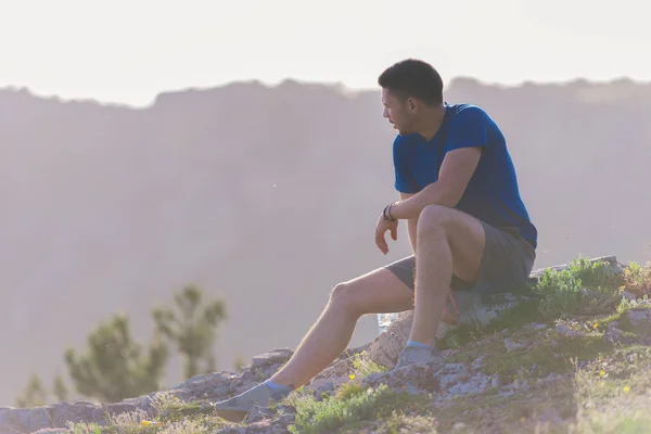 Knappe atleet zittend op een rotsachtige piek terwijl het kijken naar de BR — Stockfoto