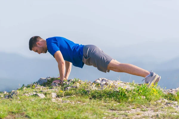 Młody sprawny mężczyzna sportowiec robi push-upy na zewnątrz na klifie w — Zdjęcie stockowe