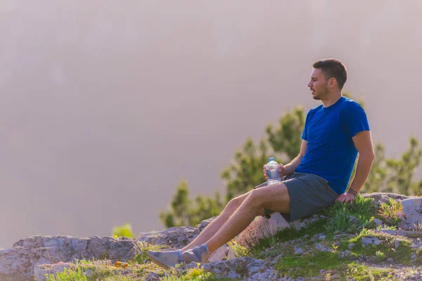 英俊的运动员坐在岩石峰,而看着br — 图库照片