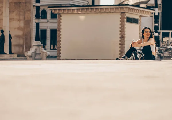 Menina de patinação em linha sentada nas escadas na praça da cidade — Fotografia de Stock