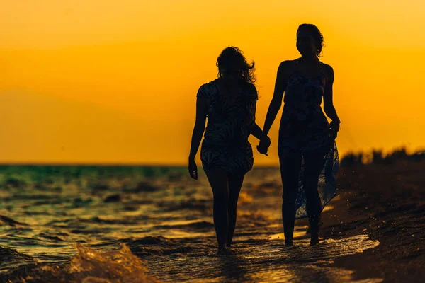 Silhouet meisjes wandelen op het strand met uitzicht op zee — Stockfoto