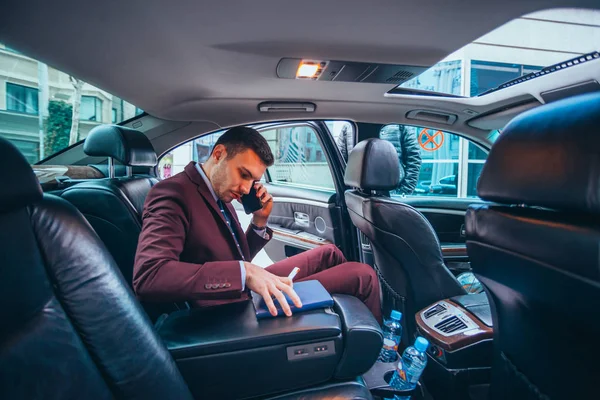 Empresario sentado en una limusina mientras habla por teléfono leyendo — Foto de Stock