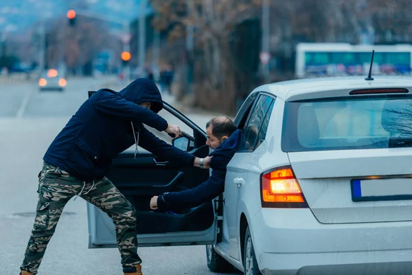 El ladrón de coches está sacando al dueño del coche de su coche y tratando de — Foto de Stock