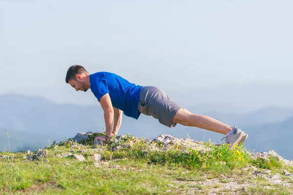 Młody sprawny mężczyzna sportowiec robi push-upy na zewnątrz na klifie w — Zdjęcie stockowe