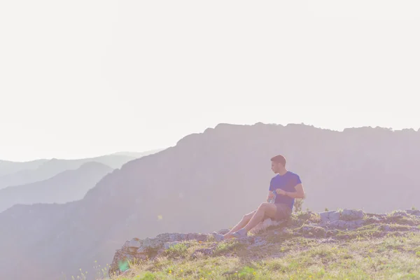 Schöner Athlet sitzt auf einem felsigen Gipfel, während er die br — Stockfoto
