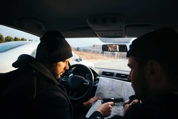 Criminales sentados al atardecer en un coche, mirando el mapa de la ciudad y — Foto de Stock