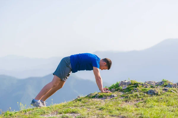 Um jovem atleta masculino está fazendo flexões ao ar livre em um penhasco w — Fotografia de Stock