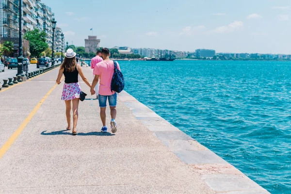 Cute couple walking by the sea on a boardwalk while the girl hol — Stock Photo, Image