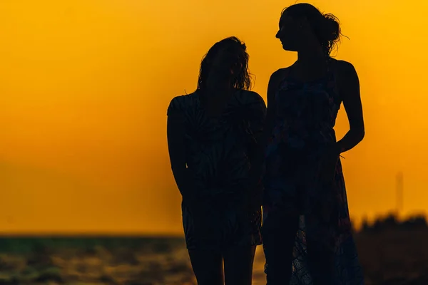 Vrouwen in jurk lopen op het strand bij zonsondergang tijd — Stockfoto