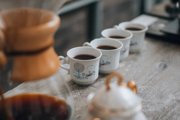 Ahşap sehpanın üzerinde dört beyaz kahve fincanı ve bulanık Cafe Backgroun — Stok fotoğraf