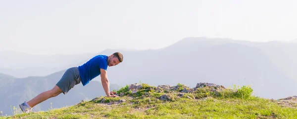 A young fit male athlete is doing push-ups outdoors on a cliff w — Stock Photo, Image