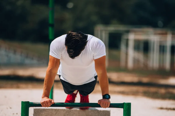 Mannelijk fitness model cross-training op metalen bars op het strand — Stockfoto