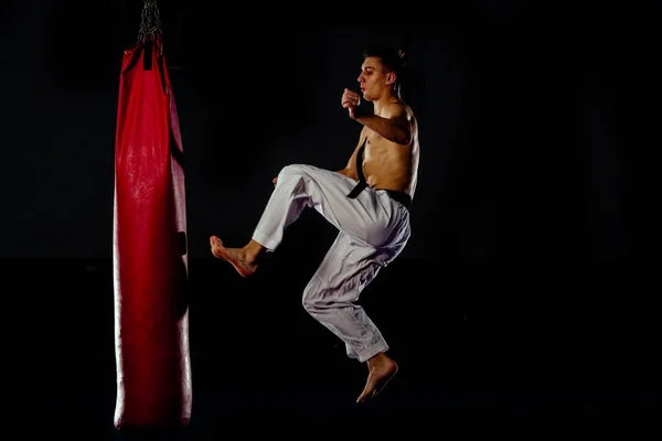 Fit karate hombre pateando en saco de boxeo en el gimnasio — Foto de Stock