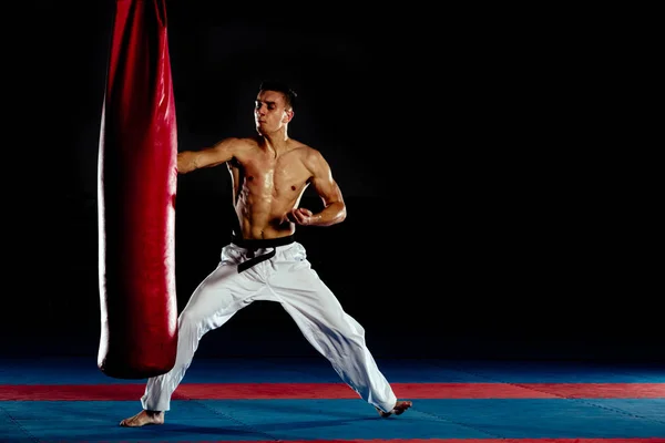 Boxeador golpeando agresivamente con una patada una bolsa de arena aislada en bl — Foto de Stock