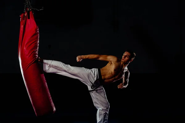 Man hitting the punching bag on black background — Stock Photo, Image
