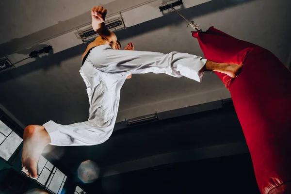 Uomo muscolare calcio boxe con sacco da boxe rosso in palestra — Foto Stock