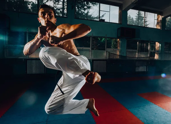 Hombre atlético pateando saco de boxeo con pierna, entrenamiento kickboxing — Foto de Stock