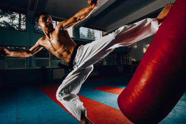 Jovem homem forte chutando saco de perfuração durante seu treinamento — Fotografia de Stock