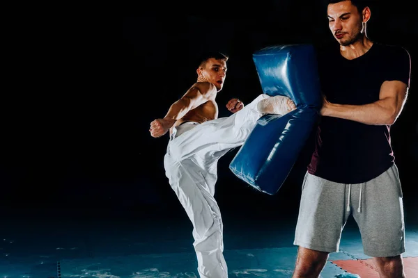 Caucásico joven sosteniendo un saco de boxeo mientras su amigo patea — Foto de Stock