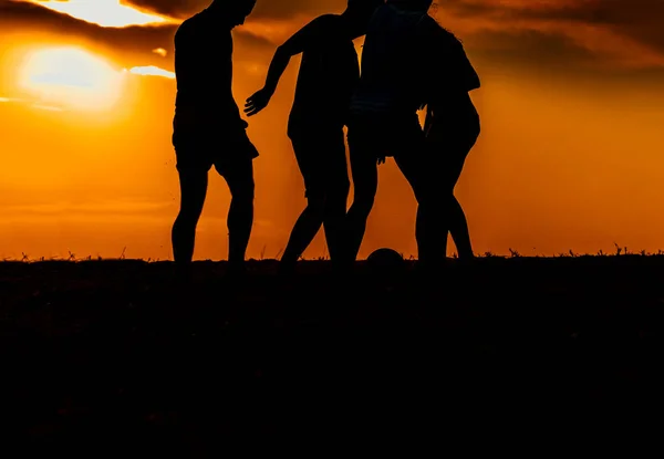 Amigos silhueta jogando futebol na praia de areia — Fotografia de Stock