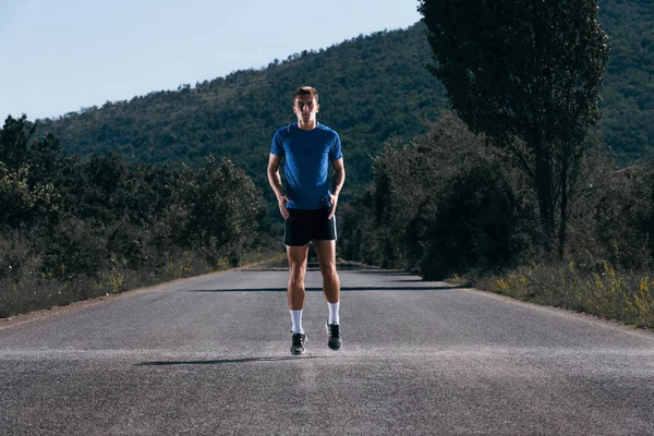 Mannelijke atleet loopt op een lege weg in het bos, terwijl het proberen — Stockfoto