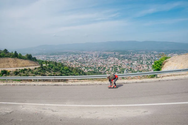 Männlicher Hipster mit Hut und rotem Hemd reitet auf einem Longboard — Stockfoto