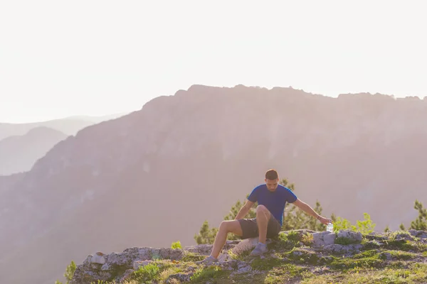 Knappe atleet zittend op een rotsachtige piek terwijl het kijken naar de BR — Stockfoto
