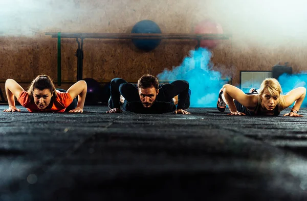 Tres personas haciendo flexiones en el entrenamiento en el gimnasio —  Fotos de Stock