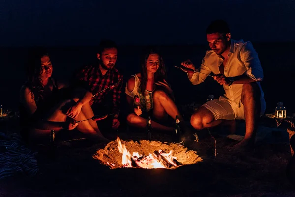 Grupo de amigos que se divertem na praia sentados ao redor do fogo — Fotografia de Stock