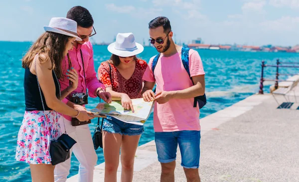 Junge Männer und Frauen lächeln und versuchen, die Karte der Touristenorte zu lesen. — Stockfoto