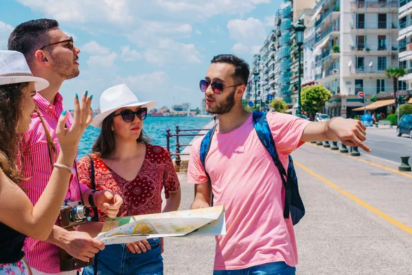 Junge Männer und Frauen lächeln und versuchen, die Karte der Touristenorte zu lesen. — Stockfoto