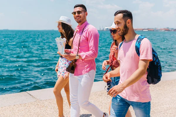 Vier Touristen, die am Meer spazieren, während sie eine Landkarte lesen und — Stockfoto