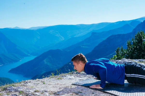 强壮英俊的金发运动员在山顶上做俯卧撑 同时欣赏山谷中湖面的迷人景色 — 图库照片