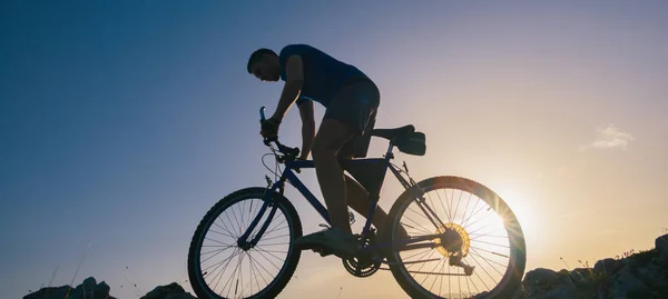 Silhouette di un mountain bike in forma maschile in sella alla sua moto in salita o — Foto Stock