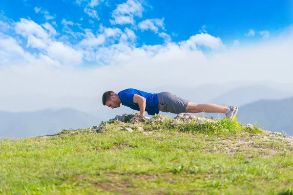 Um jovem atleta masculino está fazendo flexões ao ar livre em um penhasco w — Fotografia de Stock