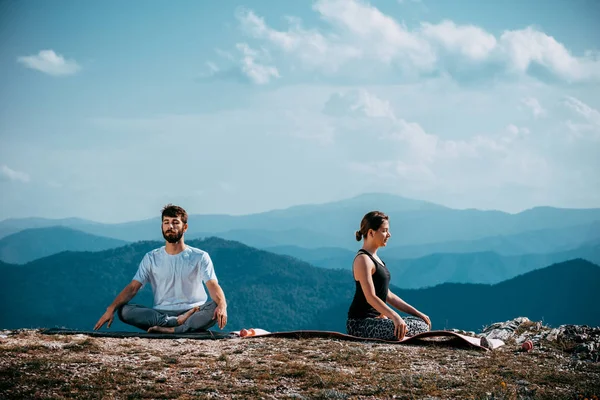 若い女性と男が山の間でヨガを練習 — ストック写真