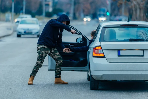 El ladrón de coches está sacando al dueño del coche de su coche y tratando de —  Fotos de Stock