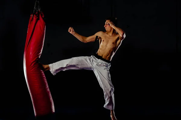 Homem atlético chutando saco de perfuração com perna, kickboxing treinamento — Fotografia de Stock