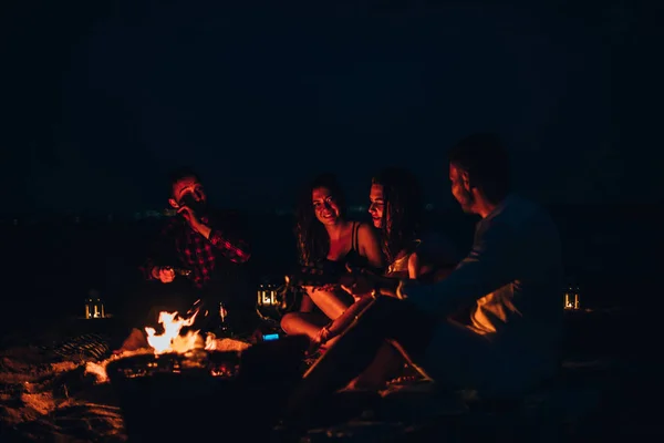 Grupa przyjaciół imprezuje na plaży siedząc przy ognisku — Zdjęcie stockowe