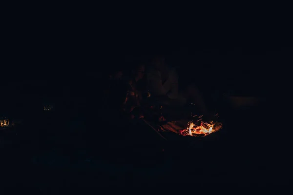 İnsanlar geceleri sahilde parlak bir şenlik ateşi etrafında oturup — Stok fotoğraf