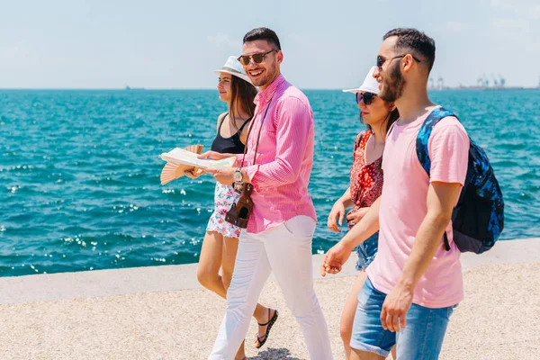 Fyra turister som går bredvid havet medan du läser en karta och de — Stockfoto