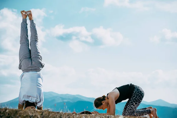 美しいです若いですカップルMeditingでヨガポーズでA大川に対して劇的な空 — ストック写真