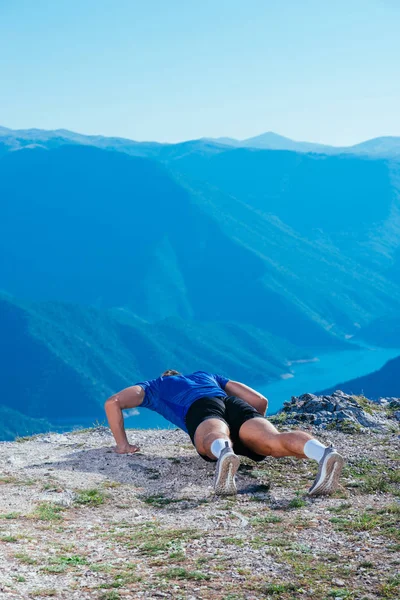 英俊的运动员站在悬崖边上时穿着运动服 适合做跳跃和俯卧撑 — 图库照片