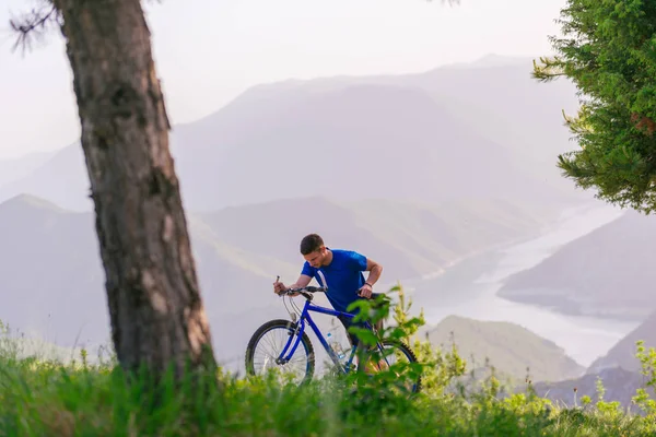 穿着蓝色衬衫的山地自行车手正在推动他的自行车通过 — 图库照片