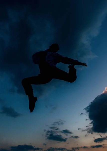 저녁에 구름낀 하늘로 점프하는 잘생긴 남자의 실루엣 — 스톡 사진